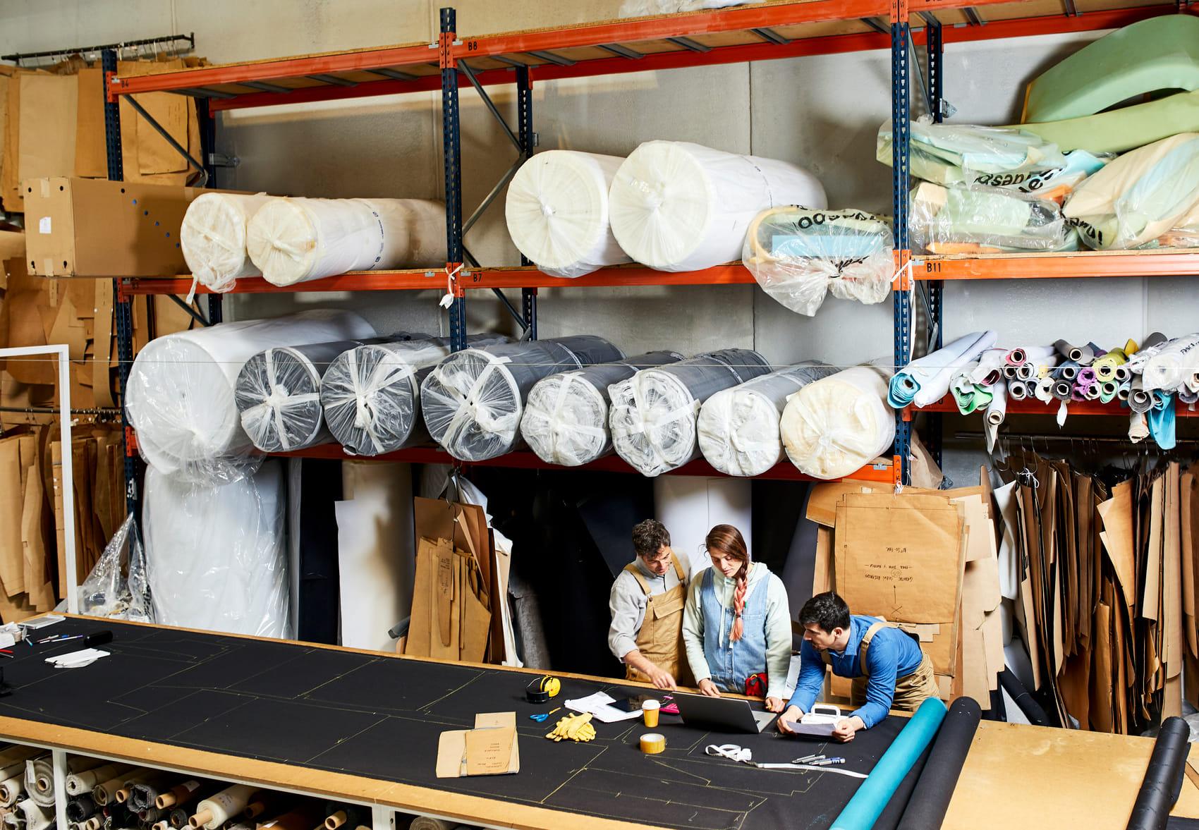 Drie mensen staan aan de ontwerptafel van een stoffenfabriek en hebben overleg.